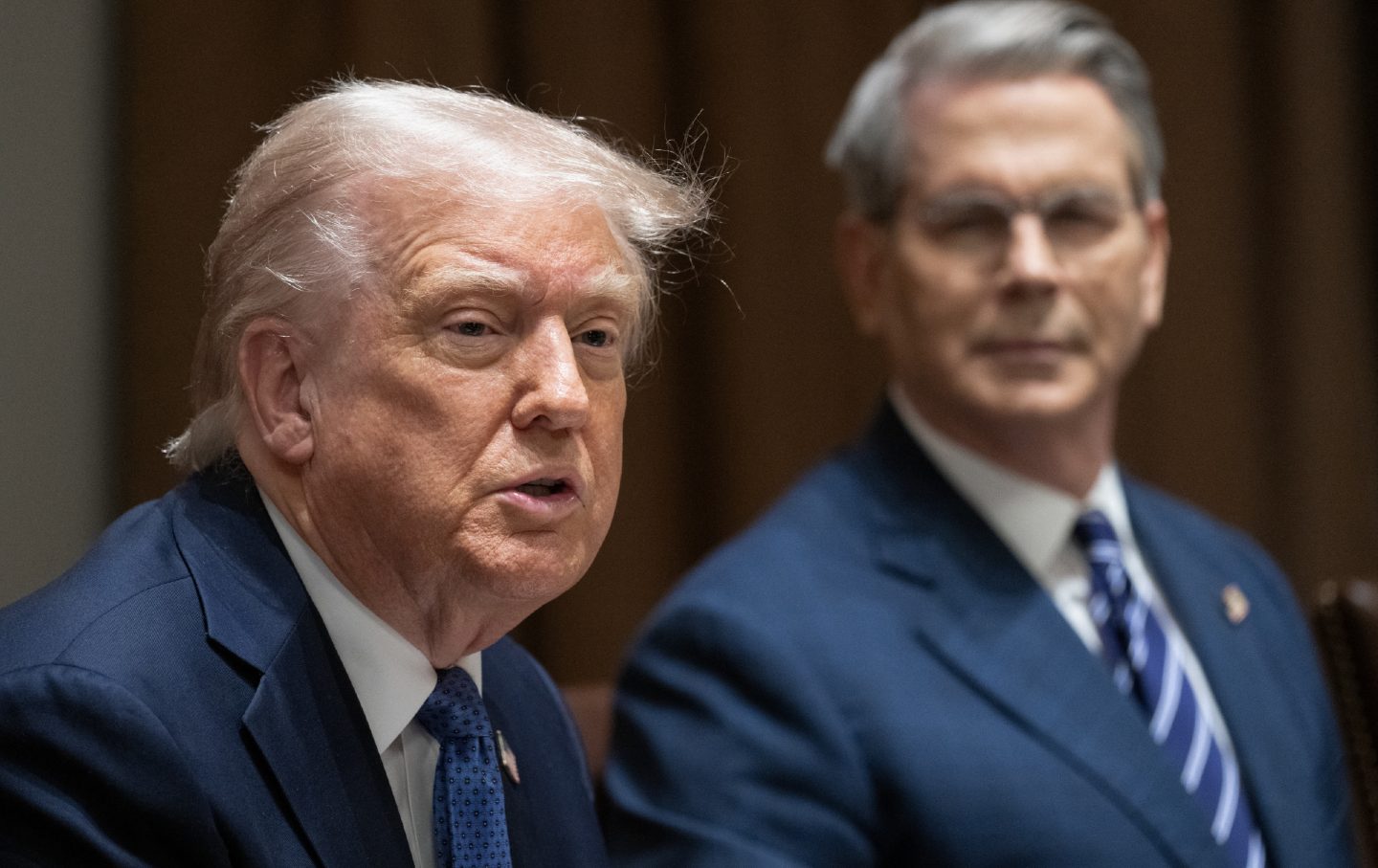 Trump speaks in the foreground while Treasury Secretary Scott Bessent watches behind him.